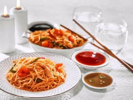 On a plate yummy prawn noodles served with tomato sauce, chili sauce, chopsticks, and water