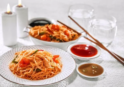 Delicious steaming Chinese noodles served in a plate with two sauce and chopsticks on a table.