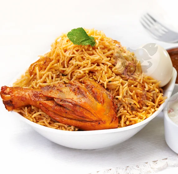 A bowl full of delicious chicken biriyani with one leg piece, fried onions, raita, egg, and gravy