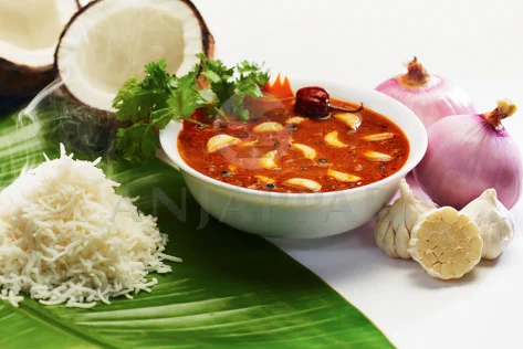 A bowl of garlic tangy curry with hot steamed rice served on a banana leaf accompanied with onion.