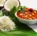 A bowl of garlic tangy curry with hot steamed rice served on a banana leaf accompanied with onion.