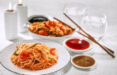 Two plates of Chinese noodles with tomato and chili sauce, chopsticks, and two glasses of water