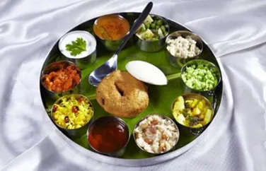 A plate full of delicious varieties of rice, gravies, vegetables, curd, idly, and vada with a spoon