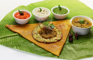 On a banana leaf, a dosa topped with omelette and gravy with sambar and three types of chutney