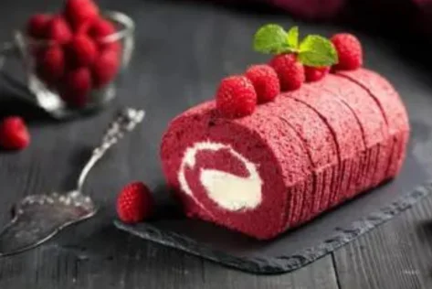 A scrumptious red velvet cake roll garnished with fresh raspberries and mint leaves with a spoon.