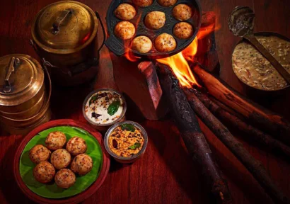 Warm kuli paniyaram cooked on a traditional firewood stove served on a clay plate with two chutneys