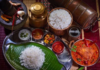 A bowl of fish curry is served with a variety of dishes and rice presented with fragrant spices