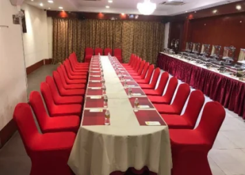 A beautifully decorated long table with red chairs and water bottle, ready for an elegant gathering