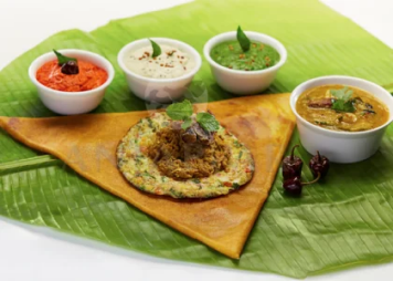 A dosa with eggs and sauce, sambar, and three kinds of chutney, served on a banana leaf